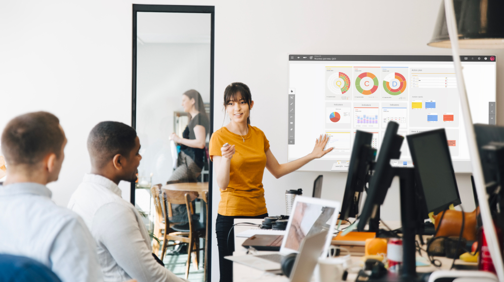 Woman presenting Digital Visual Management board to showcase VUCA via QCD information for collaboration and business optimization