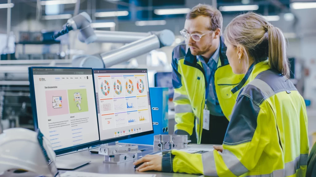Alt Plant manager and team member using digital QCD board to visualize safety metrics on the shop floor of a Lean Manufacturing plant.