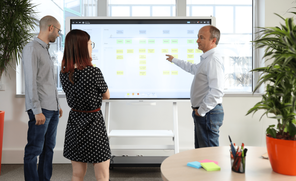 Équipe autour d'une table lors d'une réunion utilisant un écran tactile avec l'outil de gestion visuelle iObeya pour une collaboration optimisée.