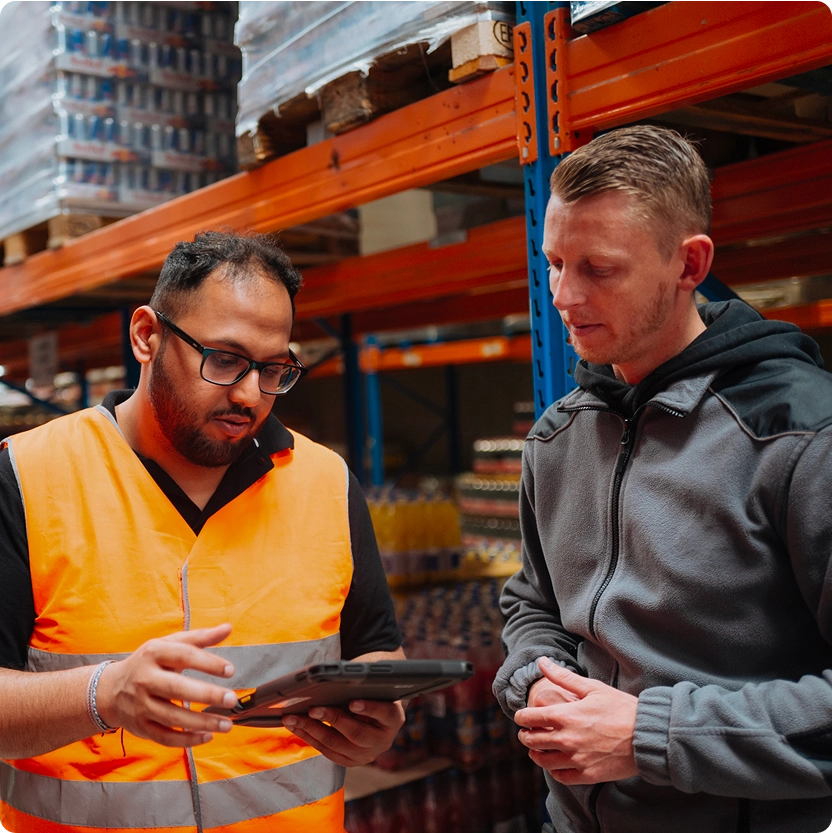 Two manufacturing workers reviewing production data on a tablet in a warehouse, illustrating collaboration and digital performance management with iObeya.